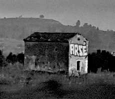 A small concrete storage shed of some kind with the word ARSÉ spray painted in block lettering above its entrance.