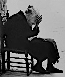 An old black and white photograph of a white-haired hunch-backed Spanish woman of about 80 or so dressed all in black, seated on a small wooden chair, right side on, head bowed, her left hand held to her weary brow in what appears to be a deeply despondent gesture expressing much mental anguish. Or perhaps it was just a very hot day that day.